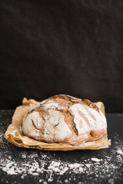 Rustiek eigengemaakt gebakken brood op pakpapier tegen zwarte achtergrond