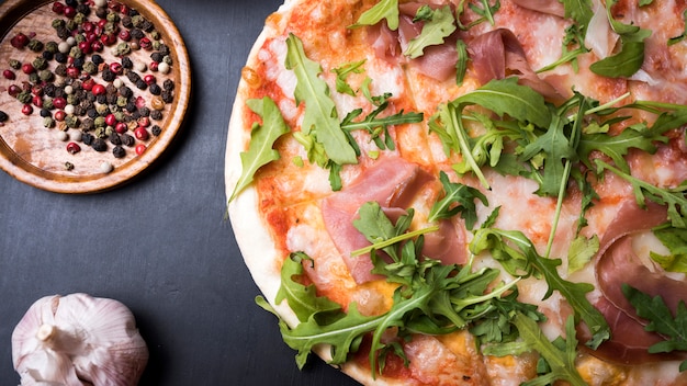 Ruwe baconpizza met zwarte peper en knoflookbol over zwarte oppervlakte