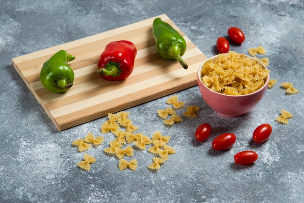 Ruwe bogen pasta met groenten op een houten bord.