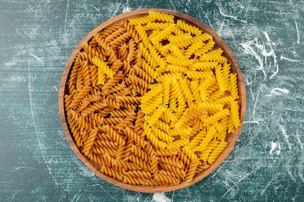 Ruwe fusilli pasta in een houten dienblad, op het blauwe oppervlak