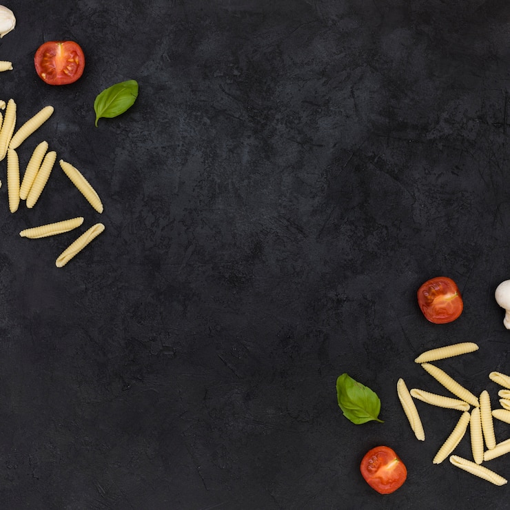 Gratis Foto ruwe garganellideegwaren met gehalveerde tomaten en basilicum op de hoek van de zwarte geweven achtergrond