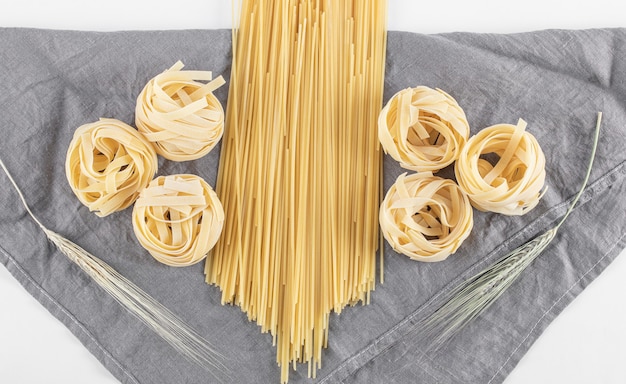 Ruwe tagliatelle en spaghettideegwaren op grijs tafelkleed.