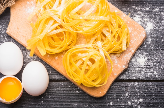 Gratis foto ruwe tagliatelle op hakbord met gebroken en hele eieren op houten tafel