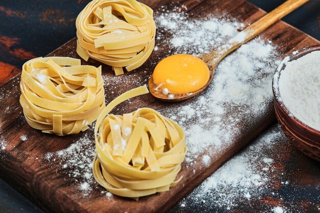 Ruwe tagliatelle pasta op een houten bord met kom poeder.