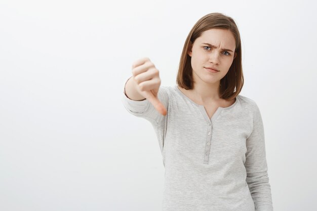 Saai en niet indrukwekkend verhaal. Portret van niet onder de indruk ontevreden kieskeurig meisje met kort bruin kapsel fronsend lippen tuit van afkeer tonen duim naar beneden afkeer en antipathie uiten