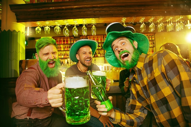 Gratis foto saint patrick's day-feest. gelukkige vrienden vieren en drinken groen bier. jonge mannen en vrouwen die groene hoeden dragen. pub interieur.