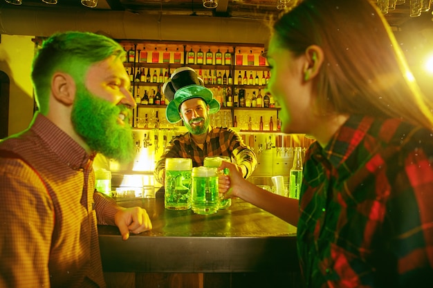 Saint Patrick's Day-feest. Gelukkige vrienden vieren en drinken groen bier. Jonge mannen en vrouwen die groene hoeden dragen. Pub interieur.