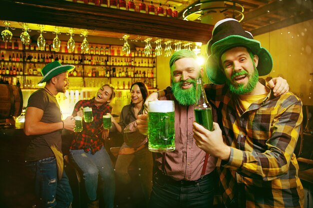 Saint Patrick's Day-feest. Gelukkige vrienden viert en drinkt groen bier. Jonge mannen en vrouwen die groene hoeden dragen. Pub interieur.