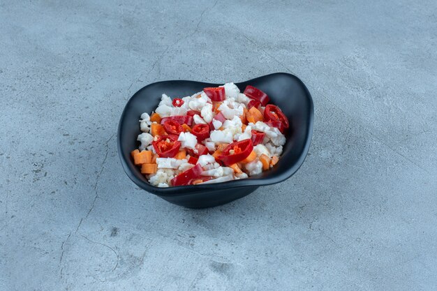 Salade gemaakt van bloemkool, peper en wortelen in een zwarte kom op marmer.