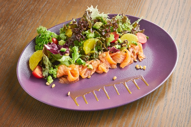 Salade met zalm, mix van bladeren, cherrytomaatjes op paarse plaat. handig en gezond eten.