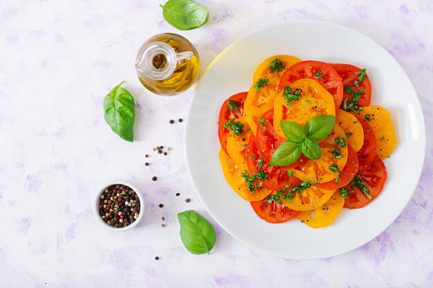 Salade van gele en rode tomaat met basilicumpesto op een lichte lijst. Plat liggen. Bovenaanzicht