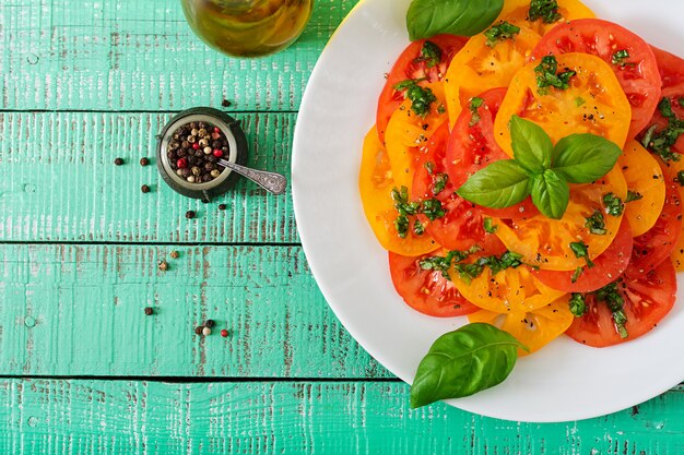 Salade van gele en rode tomaat met basilicumpesto op een lichte lijst. Plat liggen. Bovenaanzicht