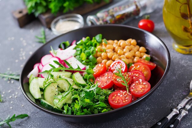 Salade van kikkererwten, tomaten, komkommers, radijs en greens. Dieetvoeding. Boeddha schaal. Veganistische salade.