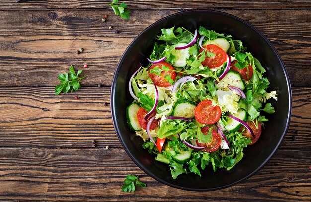 Salade van tomaten, komkommer, rode uien en slabladeren. Gezond zomervitaminemenu. Veganistisch plantaardig voedsel. Vegetarische eettafel. Bovenaanzicht Plat leggen