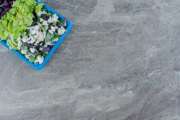 Salademix van bloemkool, kool en amarant op een blauwe schaal op marmer.