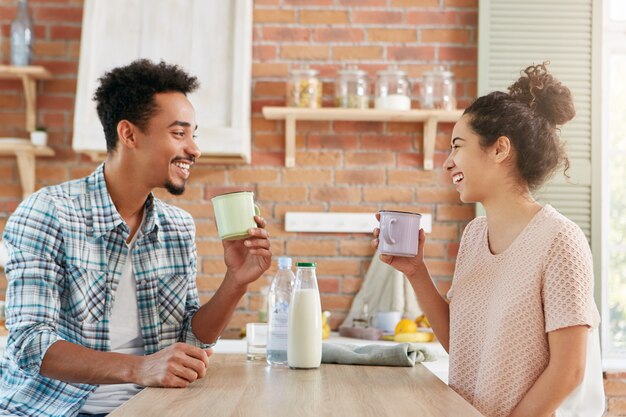 Samen thuis tijd doorbrengen. Vrolijke bebaarde man en zijn vrouw drinken 's ochtends thee of melk, hebben een goed humeur,