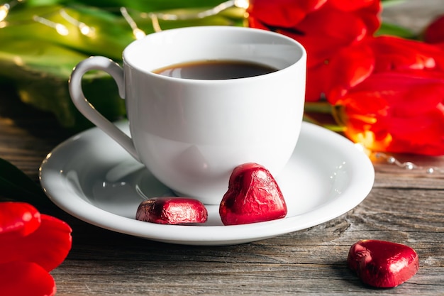 Samenstelling met een kopje koffie hartvormige snoepjes en rode bloemen close-up