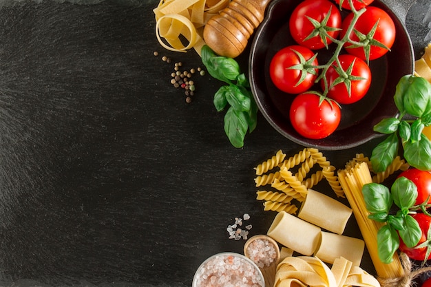 Samenstelling met verscheidenheid van pasta, tomaten en basilicum op donkere ondergrond