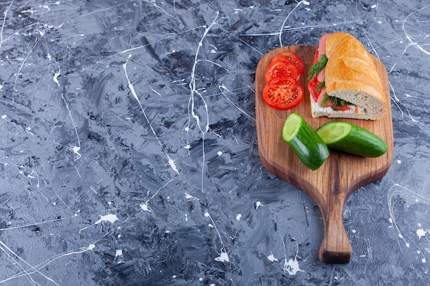 Sandwich, gesneden komkommer en tomaten op snijplank op blauw.