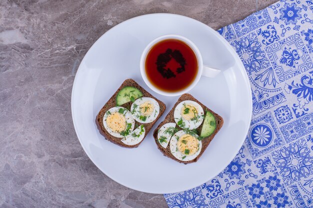 Sandwich met gekookt ei met een kopje thee in een witte plaat.