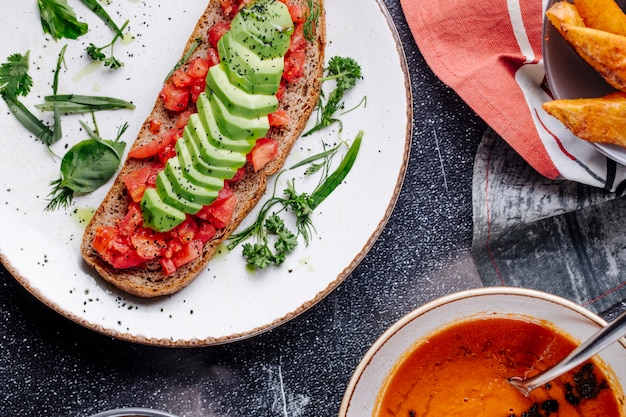 Sandwich met tomaat, komkommer en groene kruiden met een kom linzensoep.