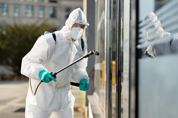 Sanitaire medewerker in hazmat-pak die openbaar gebouw desinfecteert tijdens coronavirusepidemie