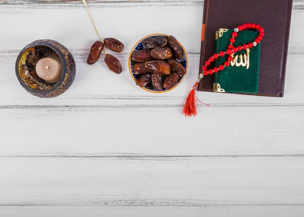 Sappige gedroogde dadels schaal; kaars; dagboek; kuran en islamitische rozenkrans gebed kralen op witte houten bureau
