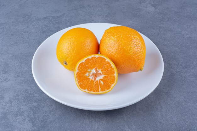 Sappige sinaasappelen op plaat op marmeren tafel.