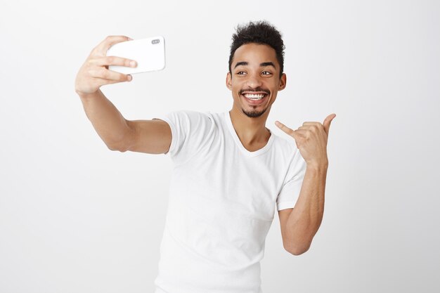 Sassy lachende Afro-Amerikaanse man selfie te nemen op smartphone, yolo gebaar tonen