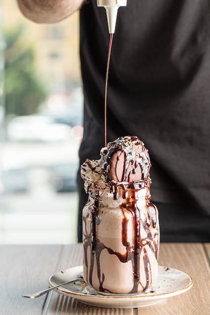 Saus toevoegen aan romige vanille milkshake met chocoladesaus in een witte schotel