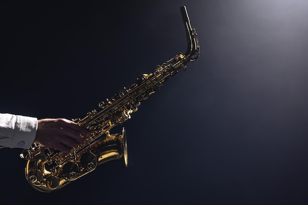 Gratis foto saxofoon in de handen van een man op een donkere achtergrond kopie ruimte