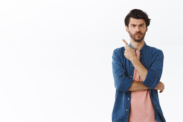 Sceptisch onzeker knappe man in roze t-shirt shirt fronsend grimas peinzend en onzeker hebben twijfels wijzend linker bovenhoek niet zeker kopen of geen advies vragen denken en aarzelen