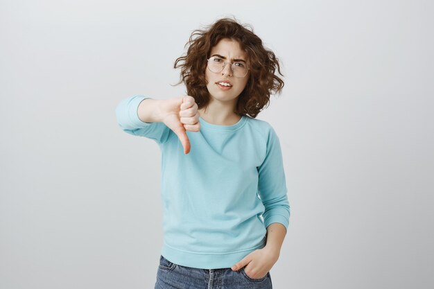 Sceptische en teleurgestelde vrouw die duimen naar beneden laat zien, een zeer slecht, vreselijk resultaat