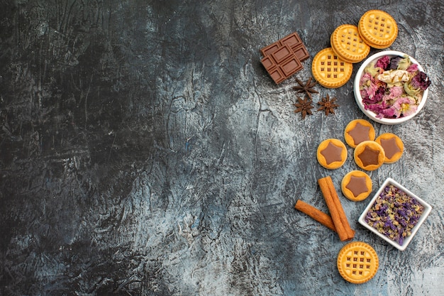 Gratis foto schalen met droge bloemen met koekjes en chocoladerepen en kaneel aan de rechterkant van grijze grond