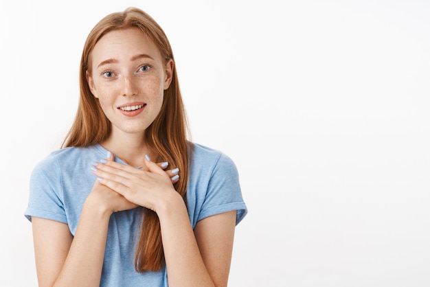 Gratis foto schattig aangeraakt gembermeisje met sproeten met palmen op hart smeltend van charmante verrassing glimlachend en starend met bewondering en genegenheid dankbaar over grijze muur