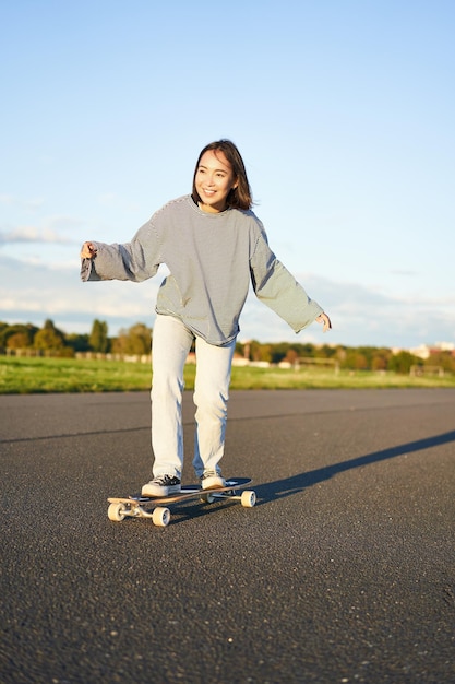 Schattig Aziatisch meisje rijden skateboard schaatsen op de weg en lachende schaatser op cruiser longboard genieten van o