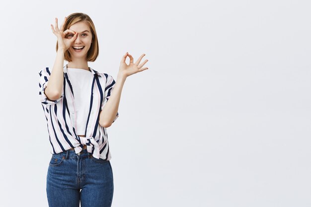 schattig blond meisje kijkt door goed gebaar met geamuseerd geïntrigeerd gezicht