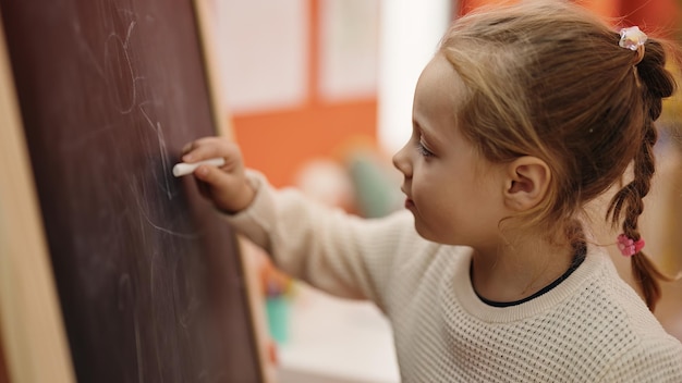 Gratis foto schattig blond meisje kleuterschool student tekenen op het bord op de kleuterschool