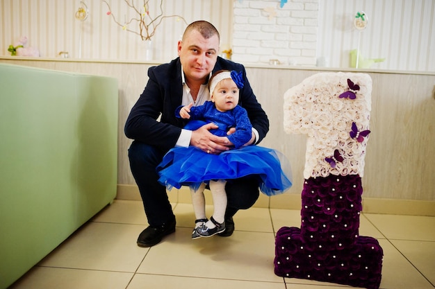 Schattig klein babymeisje bij blauwe jurk in de buurt van 1 jaar verjaardagsnummer met vader Gratis Foto