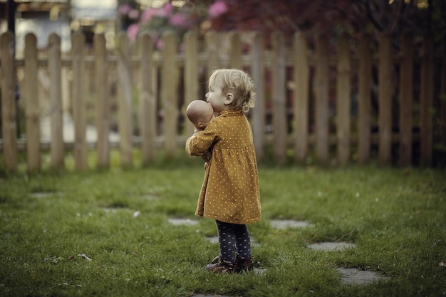 Schattig klein kind dat haar pop vasthoudt terwijl het op het met gras bedekte gazon staat