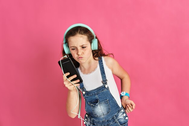 Schattig klein meisje dat naar muziek luistert met een telefoon en koptelefoon op een roze muur