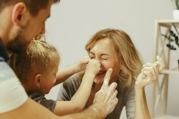 Schattig klein meisje en haar mooie ouders bereiden het deeg voor de taart in de keuken thuis