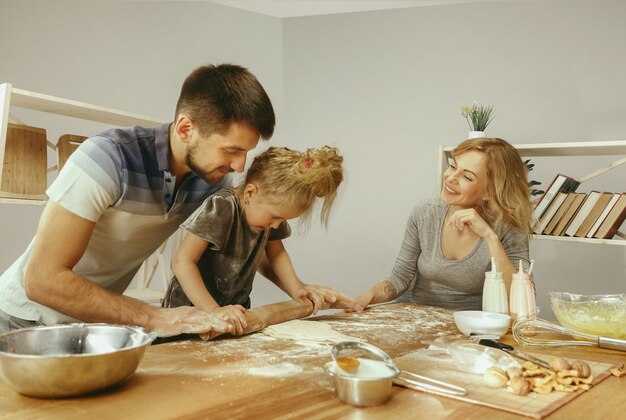 Schattig klein meisje en haar mooie ouders bereiden het deeg voor de taart in de keuken thuis