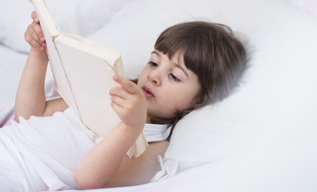 Schattig klein meisje lacht terwijl liggend in een gezellig wit bed met het concept van de rust en slaap van kinderen