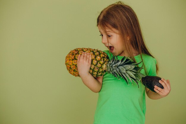 Schattig klein meisje met ananas en avocado geïsoleerd in studio