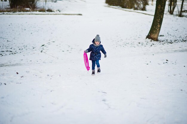 Schattig klein meisje met schotel sleeën buiten op winterdag