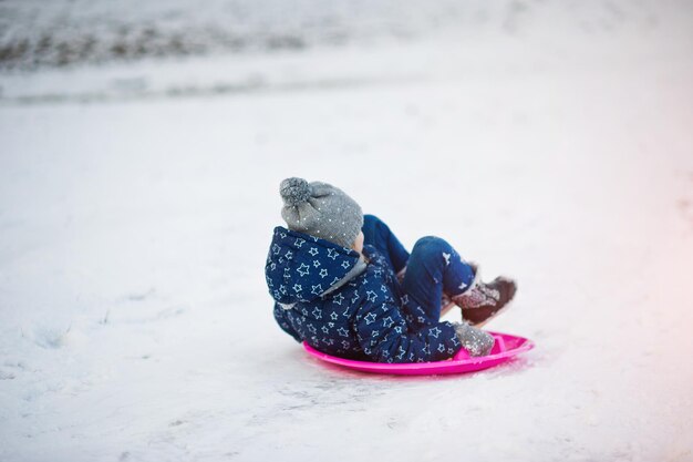 Schattig klein meisje met schotel sleeën buiten op winterdag