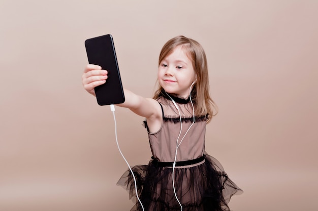 Schattig klein meisje plezier en neemt selfie. Meisje verrast in de telefoon kijken en glimlacht op geïsoleerde muur, ware emotie, goed humeur, stijlvol klein meisje