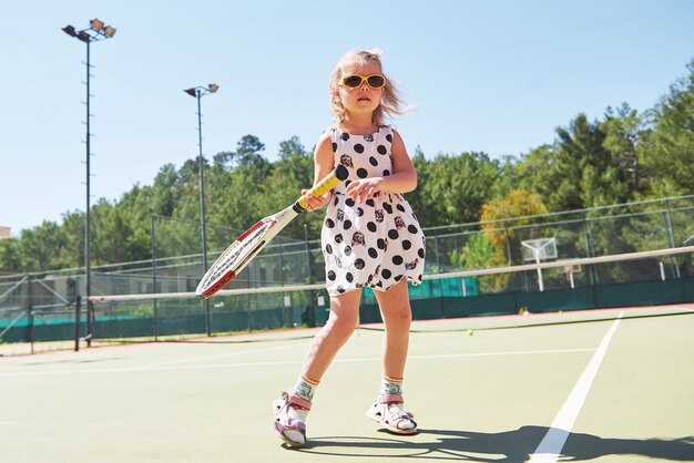 Schattig klein meisje tennissen op de tennisbaan buiten.