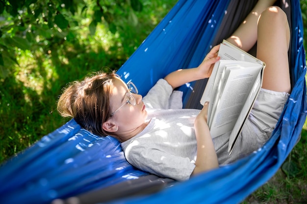 Gratis foto schattig meisje dat een boek leest in een hangmat in de tuin